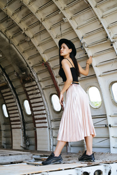 一个长头发的女人，穿着黑色和粉色的衣服，站在失事飞机的机舱里。