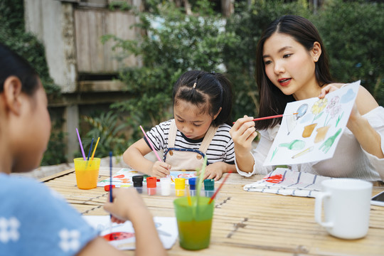 亚洲可爱的小女孩和姐姐一起在纸上用颜料和水彩画画。户外活动。