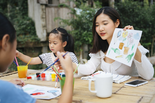 两个亚洲妹妹在纸上画水彩，坐在户外的桌子上。