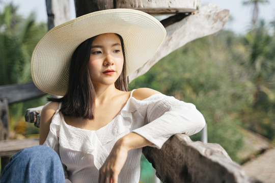一位穿着白衬衫、戴着帽子的亚洲妇女坐在乡下的长凳上。