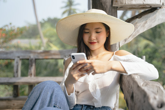 一位穿着白衬衫、戴着帽子、使用智能手机的快乐的亚洲妇女，在乡下的时候表情愉快。