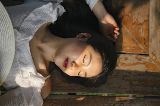 平躺-亚洲年轻女子穿着白衬衫睡在木制旧地板上。