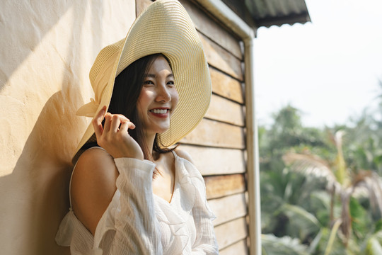 美丽的亚洲女人穿着白衬衫，戴着大帽子站在墙上。在大自然和乡村旅行。