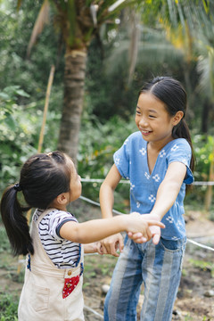 两个亚洲小女孩手牵着手在乡下的农场玩。在大自然中旅行。