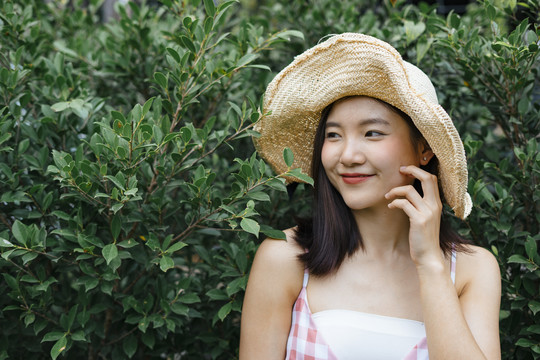 一个戴着帽子的亚洲女人站在活墙旁，旁边是一片绿叶。生态旅游。