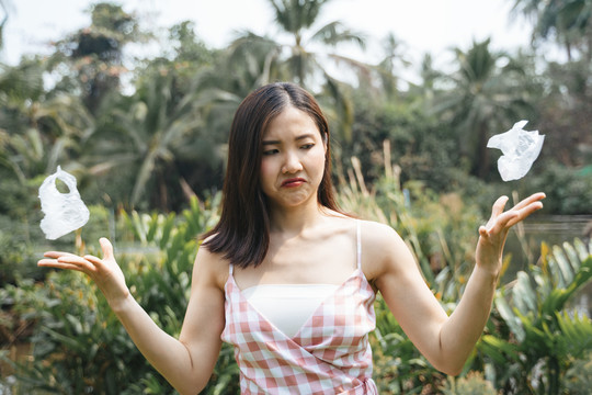 愤怒愤怒的亚洲女孩，穿着粉色连衣裙，厌恶塑料袋。拯救世界。全球变暖。从塑料垃圾中拯救地球。双手拿着皱