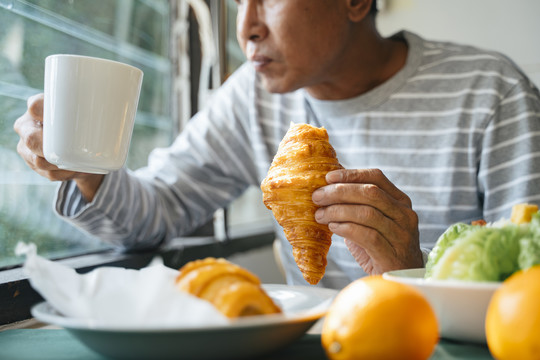 老人吃早餐时手里拿着一杯咖啡和苏珊特的剪影。