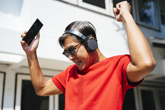 在阳光明媚的日子里，穿着红色t恤的老人在家里欣赏移动应用程序的音乐。