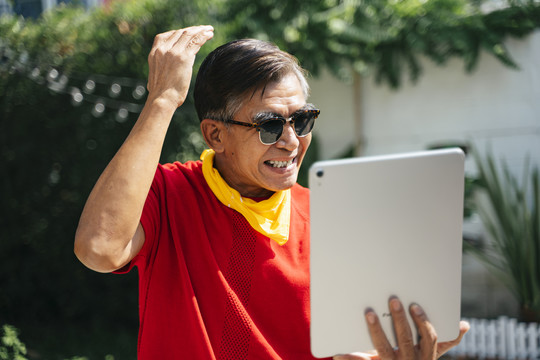 身穿红色t恤、戴着墨镜的老人看着平板电脑上的倒影，对自己的外表感到自豪。