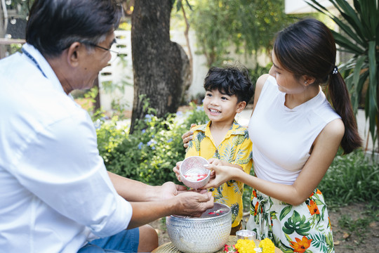 在泰国家庭日，母亲教儿子把花水浇在爷爷的手上，这是一项传统的活动。