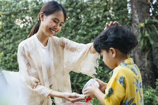 在传统节日里，母亲一边轻轻地揉着儿子的头，一边给她手上浇花水。