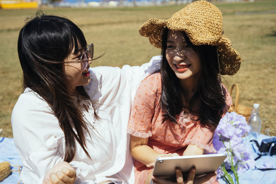 两个女孩在夏天的阳光和风中坐在田野上，一起读电子书。