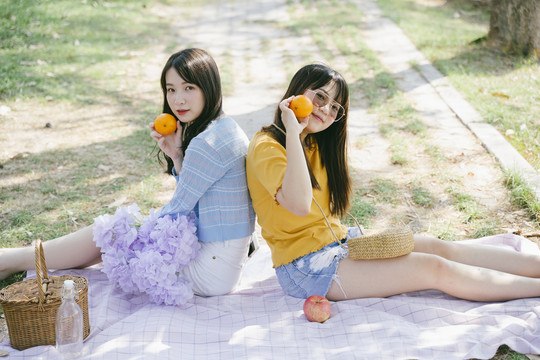 两个女孩拿着桔子坐在地上的垫子上玩耍。