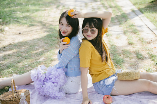 两个女孩拿着桔子坐在地上的垫子上玩耍。