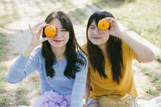 两个女孩在公园里野餐，把桔子举到眼睛上。