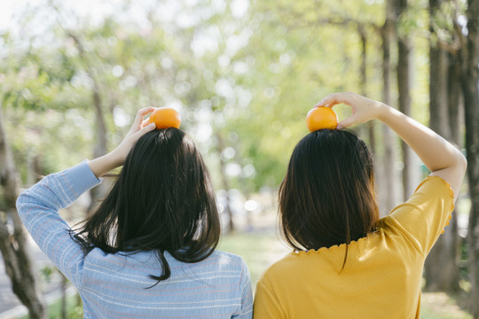 两个女孩站在一起，把桔子放在公园的头上。