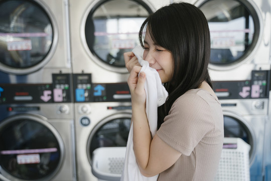 可爱的女孩抱着她从洗衣机里拿出的干净毛巾，微笑着闻了闻。