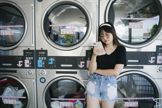 长发女孩一边用手机，一边靠着有复印空间的洗衣机。
