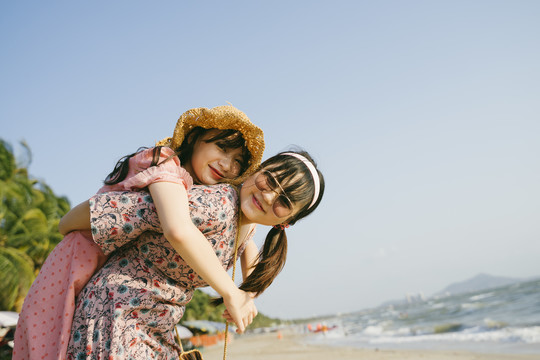 在阳光明媚的日子里，戴墨镜的女孩背着她的朋友在沙滩上散步。