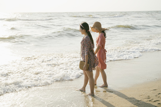 两个女孩一起走在沙滩上看着海浪。