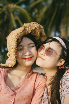 两个女孩在海滩上傍晚的阳光下脸贴在一起。