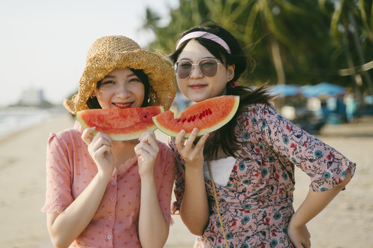 两个女孩在阳光明媚的海滩上一起吃西瓜。