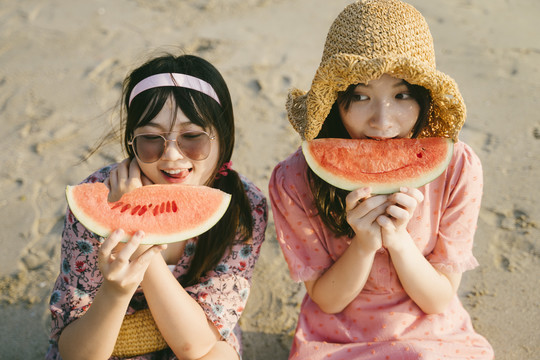 两个女孩在阳光明媚的海滩上一起吃西瓜。