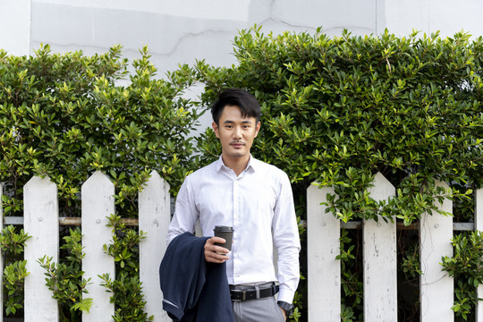 穿着白衬衫的泰国成年商人在户外拿着一杯咖啡，背景是大自然。