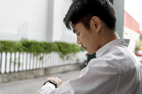 侧视特写亚泰商人在白领衬衫看手表在街上。