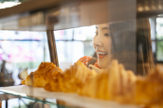 兴奋的年轻亚洲妇女看着面包店货架上的羊角面包。