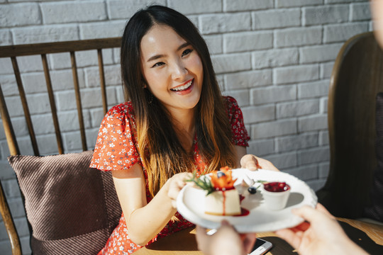 快乐的亚洲女人从甜点咖啡馆的女服务员那里拿甜点。