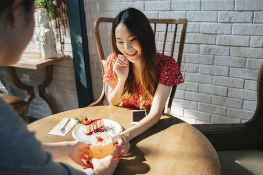 快乐的亚洲女人从甜点咖啡馆的女服务员那里拿甜点。