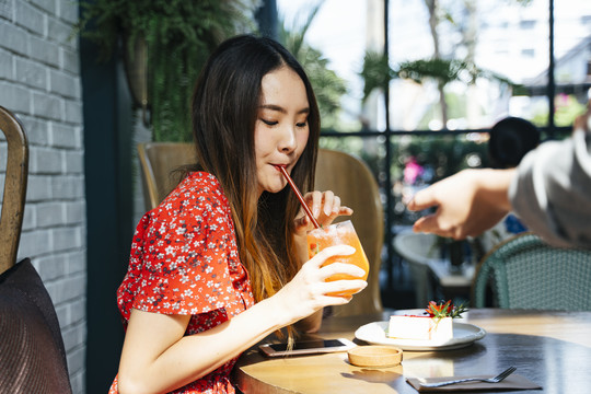 身着红色连衣裙的泰国亚裔年轻女子在咖啡馆里喝果汁。女招待要小费的手。