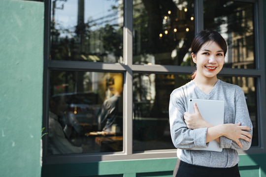 优雅的年轻女商人手持平板电脑在咖啡馆背景。