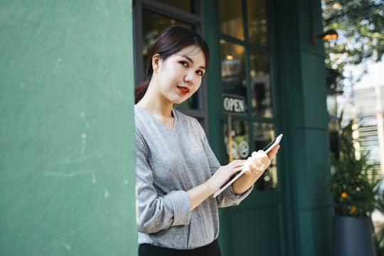 美丽的亚洲年轻女子在街上的咖啡馆背景上使用平板电脑。