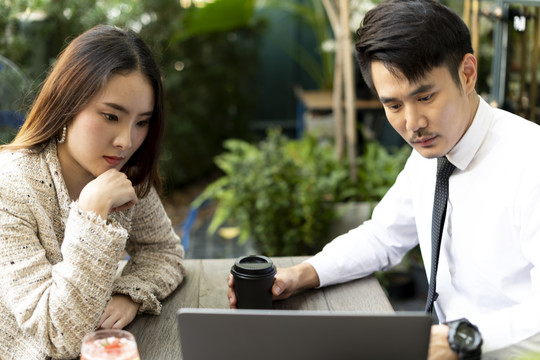 两个亚洲商人一起在咖啡店工作，看着笔记本电脑。
