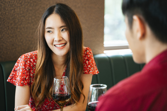 在情人节庆祝。一位穿着红裙子的美丽快乐的亚洲女人在餐馆酒吧和她的男朋友约会。