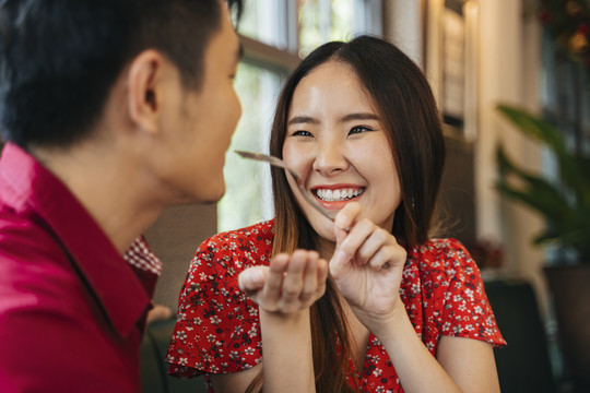 美丽的亚洲女人用叉子喂男友甜点蛋糕。