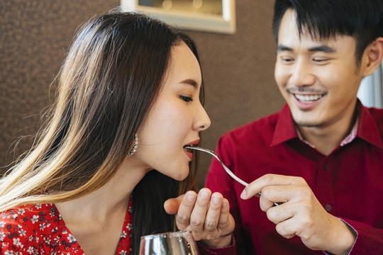 穿着红衫的泰国帅哥用叉子给他的女孩喂食物。浪漫时刻。情人节的概念。