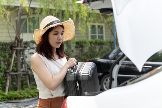 一名戴帽子的亚泰妇女打开汽车后备箱捡起旅行行李。