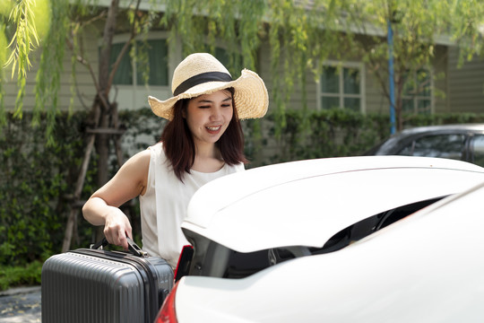 一名戴帽子的亚泰妇女打开汽车后备箱捡起旅行行李。