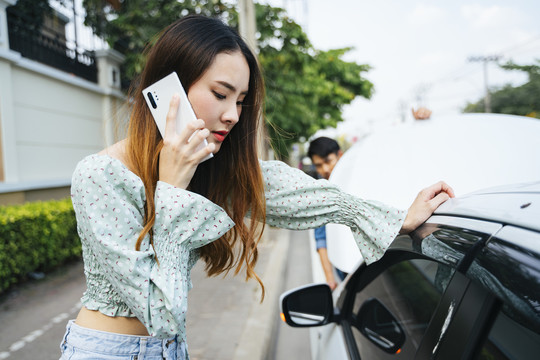 愤怒的亚洲女人开始用电话打电话给机械师来这里修车。年轻女子一边用手机一边看着街上抛锚的汽车。