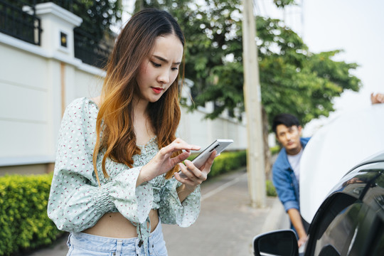 愤怒的亚洲女人开始用电话打电话给机械师来这里修车。年轻女子一边用手机一边看着街上抛锚的汽车。