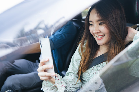 美丽的亚泰女人和她的朋友在车里旅行。使用智能手机。