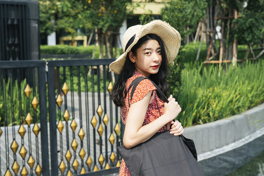 年轻漂亮的泰国亚裔旅行家女子身穿红色连衣裙，头戴红帽，在曼谷市公园旅游。