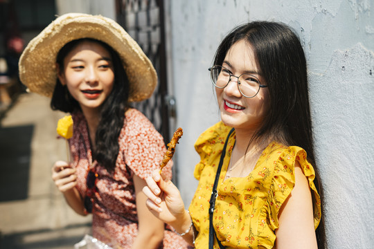 两位年轻漂亮的泰国亚裔旅行家女闺蜜一起在泰国享受街头美食。