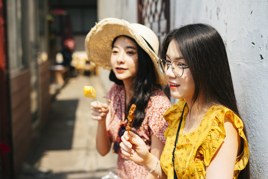 两位年轻漂亮的泰国亚裔旅行家女闺蜜一起在泰国享受街头美食。