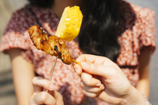 女人用烤鸡棒和菠萝欢呼。美丽的泰国女人用棍子吃街上的食物。