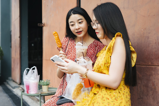 两位亚洲美女好朋友一起吃街边小吃，用智能手机自拍。