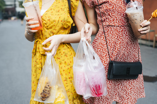 两个美丽的亚洲女人背着装满街头食物的塑料袋走在街上。